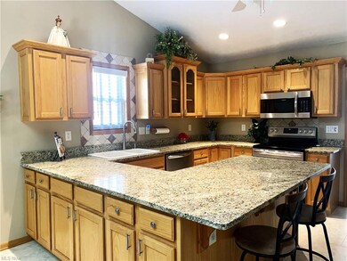 Kitchen featuring backsplash, brown cabinets, vaulted ceiling, a kitchen island, light stone countertops, stainless steel appliances, and tile floors