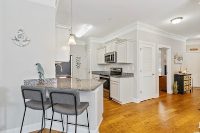 Kitchen with appliances with stainless steel finishes, a kitchen bar, dark stone countertops, a peninsula, and white cabinets