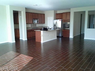 Kitchen featuring open floor plan, appliances with stainless steel finishes, a center island with sink, and brown cabinets