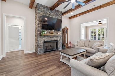 Living room with ceiling fan, wood finished floors, beamed ceiling, and a fireplace
