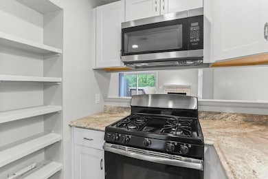 Kitchen featuring stainless steel appliances, white cabinets, open shelves, and light stone counters