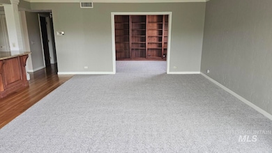 Empty room with crown molding, dark colored carpet, and dark wood-style floors