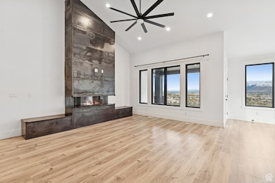 Unfurnished living room with a fireplace, light wood-type flooring, recessed lighting, high vaulted ceiling, and a ceiling fan