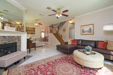 To the left of the entry, an inviting family room features fresh paint with crisp white crown molding, a stylish lighted ceiling fan, and a gas or wood burning fireplace with brick laid tile surround and a large mirror centered above.