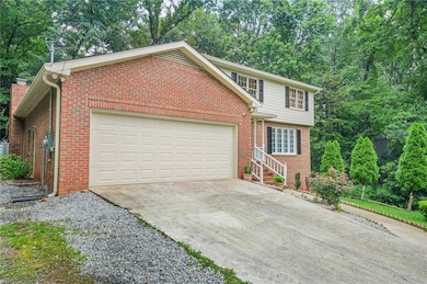 View of front of home with an attached garage, driveway, brick siding, and view of scattered trees