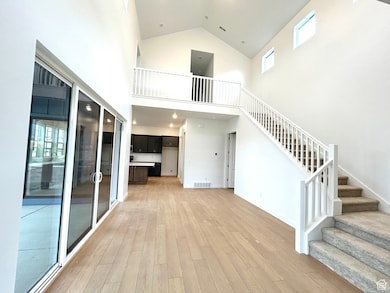 Unfurnished living room featuring high vaulted ceiling, light wood-style flooring, stairway, and recessed lighting