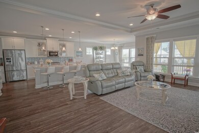 Living area featuring ceiling fan, dark wood-style flooring, crown molding, recessed lighting, and a chandelier