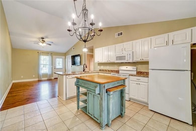 Kitchen with white appliances, white cabinets, a peninsula, ceiling fan, and a center island
