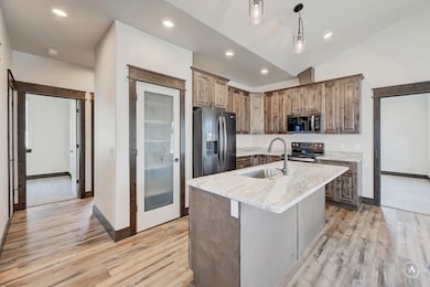 Kitchen featuring stainless steel appliances, a kitchen island with sink, recessed lighting, light stone countertops, and light wood-type flooring