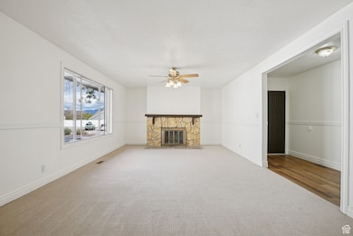 Unfurnished living room featuring carpet flooring, a fireplace, a ceiling fan, and a textured ceiling
