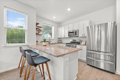 Kitchen featuring light stone counters, appliances with stainless steel finishes, light wood finished floors, white cabinets, and recessed lighting