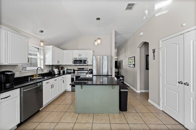 Kitchen featuring decorative light fixtures, stainless steel appliances, a kitchen island, white cabinetry, and light tile patterned floors