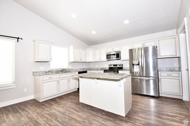 Kitchen featuring appliances with stainless steel finishes, lofted ceiling, white cabinets, dark wood finished floors, and a center island