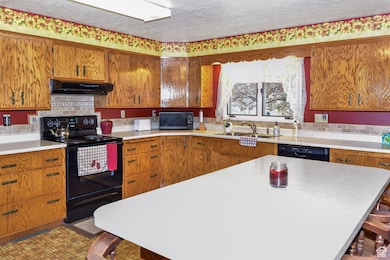 Kitchen with a kitchen bar, black appliances, brown cabinets, light countertops, and a textured ceiling
