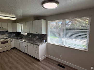 Kitchen featuring white appliances, a textured ceiling, white cabinetry, backsplash, and dark wood finished floors