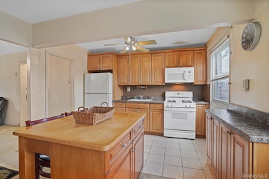 Kitchen with white appliances, light tile patterned flooring, ceiling fan, and brown cabinets