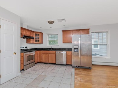 Kitchen with stainless steel appliances, brown cabinetry, under cabinet range hood, baseboard heating, and glass insert cabinets