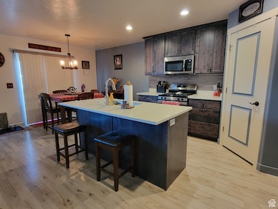 Kitchen featuring a breakfast bar area, light countertops, stainless steel appliances, a center island with sink, and dark brown cabinetry