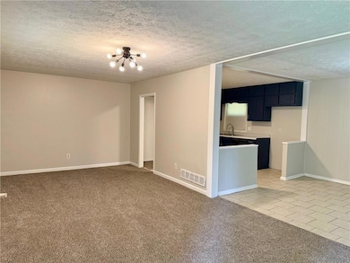 Unfurnished living room featuring a chandelier, a textured ceiling, baseboards, light carpet, and light tile patterned floors