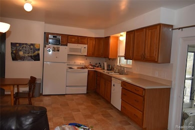 Kitchen with backsplash, white appliances, light countertops, and brown cabinetry