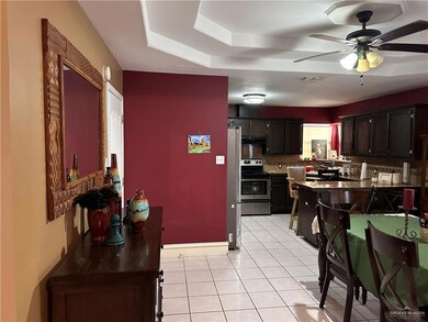 Kitchen featuring appliances with stainless steel finishes, decorative backsplash, light tile patterned flooring, ceiling fan, and a raised ceiling