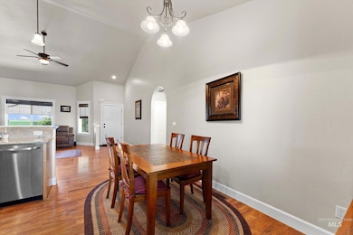 Dining area featuring arched walkways, a ceiling fan, high vaulted ceiling, light wood-style flooring, and a chandelier