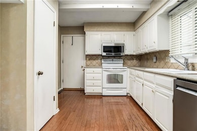 Functional kitchen with white cabinetry, laminate countertops, tile backsplash, and matching white appliances.