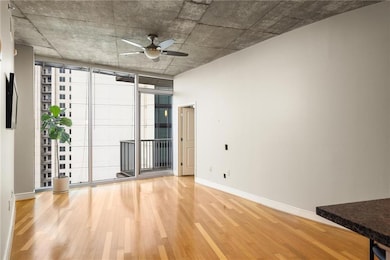 Unfurnished room featuring wood finished floors, ceiling fan, baseboards, and expansive windows