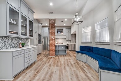 Kitchen featuring gray cabinets, glass insert cabinets, an island with sink, hanging light fixtures, and stainless steel refrigerator with ice dispenser