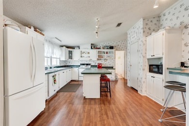 Kitchen featuring a breakfast bar area, white appliances, white cabinets, dark countertops, and wallpapered walls