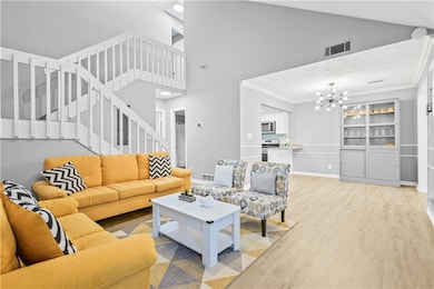 Living area featuring high vaulted ceiling, light wood-style flooring, stairs, crown molding, and a chandelier