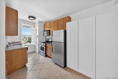 Kitchen featuring light stone counters, appliances with stainless steel finishes, light tile patterned floors, and brown cabinetry