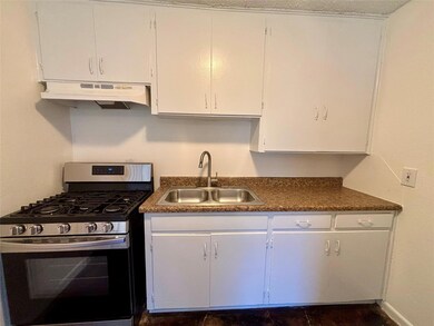 Kitchen with stainless steel gas range oven, white cabinets, under cabinet range hood, and dark countertops
