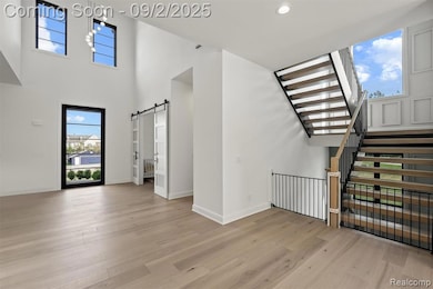 Unfurnished living room with a barn door, a towering ceiling, light wood finished floors, recessed lighting, and stairway