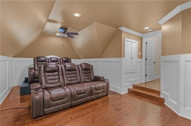 Cinema room featuring a ceiling fan, a decorative wall, wood finished floors, a wainscoted wall, and vaulted ceiling