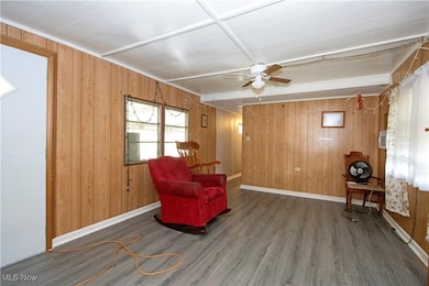 Sitting room with wooden walls, wood finished floors, and ceiling fan