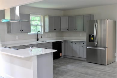 Kitchen featuring black appliances, wall chimney range hood, a sink, gray cabinets, and a peninsula