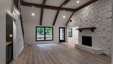 Unfurnished living room featuring beamed ceiling, a fireplace, light wood-type flooring, stairs, and high vaulted ceiling