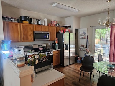 Kitchen with brown cabinets, stainless steel appliances, light countertops, dark wood finished floors, and a textured ceiling