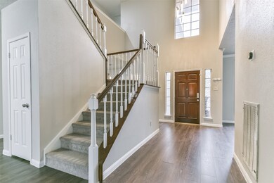 A covered front porch with a solid mahogany 6-panel front door opens into this light and bright foyer with soaring two-story ceilings, neutral grey paint, transom windows for abundant natural sunlight, a split staircase, and wood-look laminate flooring.