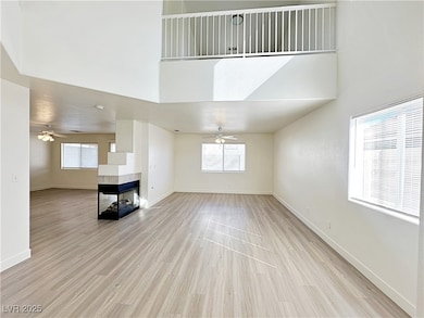Unfurnished living room with a fireplace, light wood-type flooring, a towering ceiling, and a ceiling fan