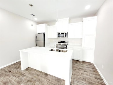 Kitchen with appliances with stainless steel finishes, decorative light fixtures, and an island with sink