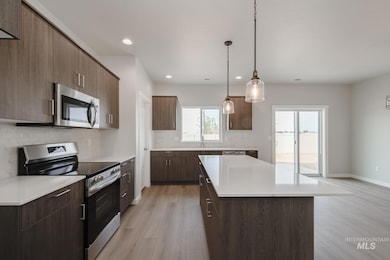 Kitchen with appliances with stainless steel finishes, modern cabinets, light wood-style floors, decorative light fixtures, and decorative backsplash
