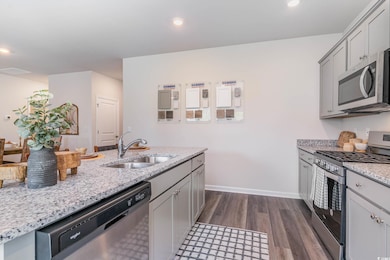 Kitchen with appliances with stainless steel finishes, dark wood finished floors, gray cabinets, light stone counters, and recessed lighting