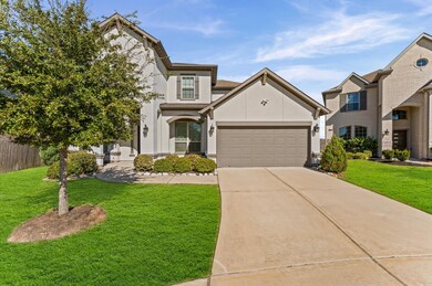 Spacious driveway leading to a two-car garage. The landscaping is well-maintained, with a tree and shrubs adding curb appeal.