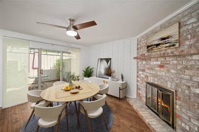 This picture was virtually staged. This cozy dining area features a warm brick fireplace, elegant wood flooring, and ample natural light from sliding glass doors leading to a patio. A ceiling fan provides comfort, and a stylish dining set offers space for gatherings.