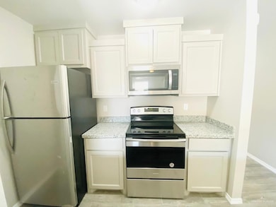 Kitchen with appliances with stainless steel finishes, white cabinets, and light stone counters