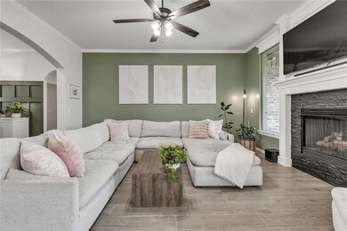 Living area with ornamental molding, arched walkways, wood finished floors, a fireplace, and ceiling fan