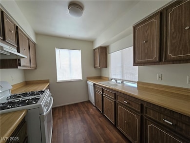 Kitchen featuring white appliances, healthy amount of natural light, dark wood-style flooring, and dark brown cabinetry