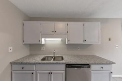 Kitchen with stainless steel dishwasher, white cabinetry, and light stone counters